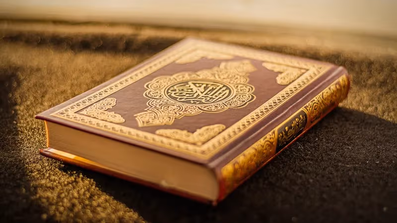 Person holding a small Quran with hands raised in quiet dua